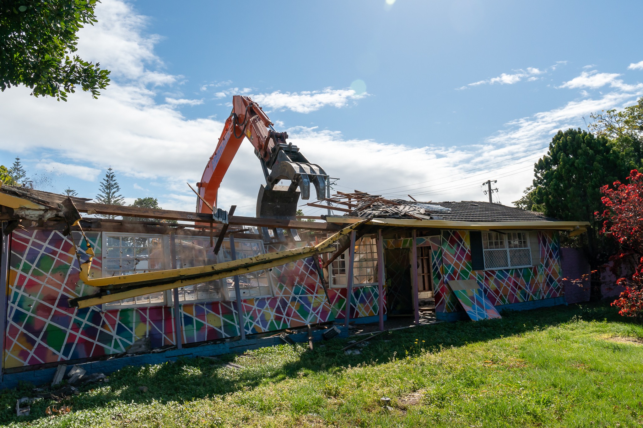 A large excavator in the midst of demolishing a colourfully painted house. 
